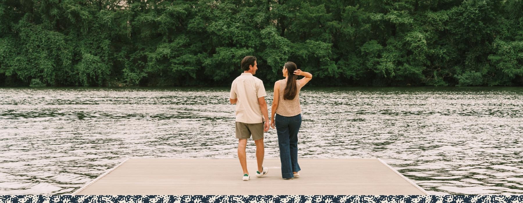 a man and woman walking on a dock by water